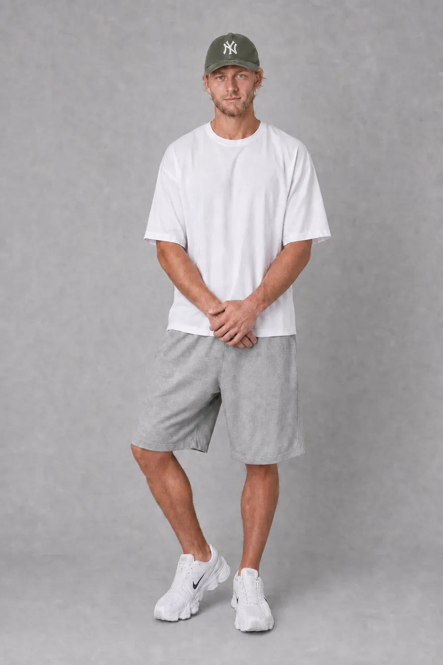 KI-generiertes On-Model-Bild: Model in weißem Oversize-Shirt, Cap und grauen Shorts